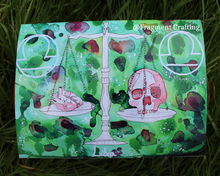 Load image into Gallery viewer, A print copy of a Libra star sign watercolour painting with various shades of green background and white set of scales with a skull one side and a heart on the other side of the scales being showed off on the grass.
