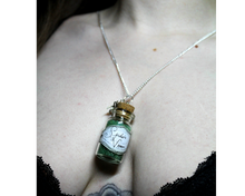 Load image into Gallery viewer, A close up of a woman wearing a silver necklace with a leaf and small corked bottle of green crystals with the bottle labelled Spider&#39;s Venom.
