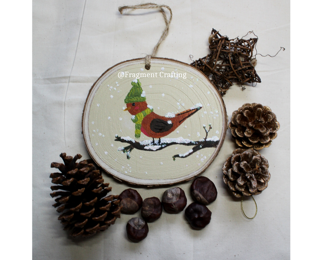 Wooden Christmas decoration of a robin sitting on a snowy branch wearing a green hat and scarf.