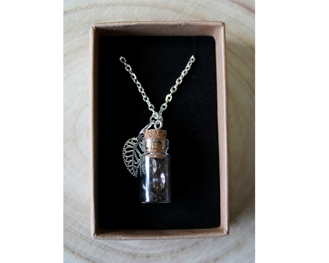 A boxed silver necklace with a leaf and small corked bottle of smokey quarts crystals.